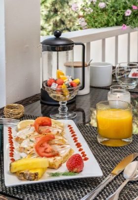 Glass top wicker table outside on a patio with breakfast plate, orange juice, coffee and dish of fresh fruit