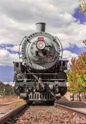 Front of a train sitting on a track with trees nearby and cloudy blue skies above