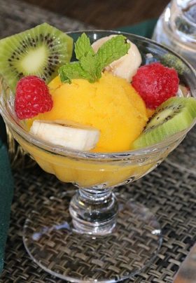 Glass dish with yellow sorbet and slicked kiwi, bananas, raspberries and a mint leaf