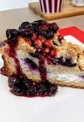 One slice of blueberry crumble pie with blueberry compote topping on a white plate