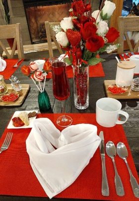 Breakfast table set for Valentine's Day with red placemats, vase of red roses and napkins folded into hearts