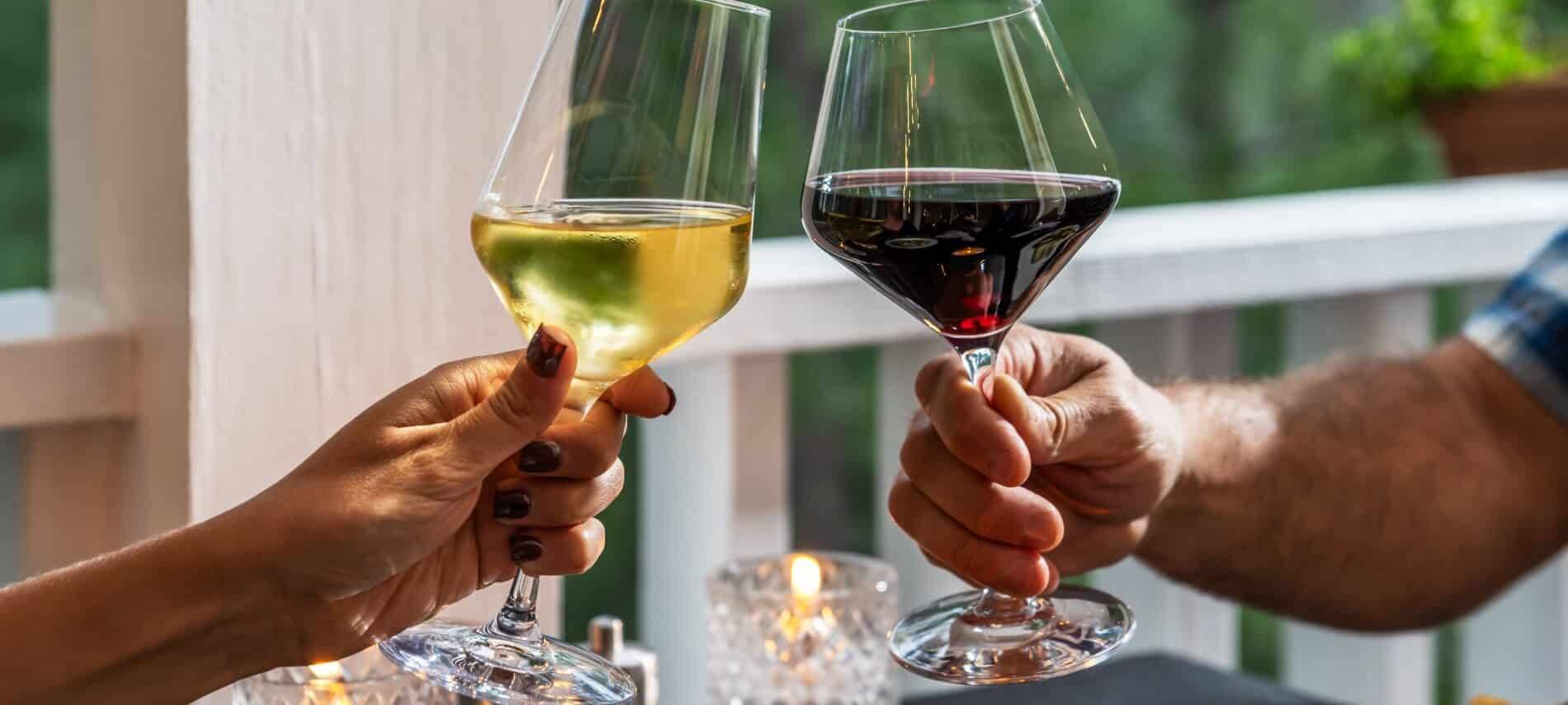 a couple holding a red and a wine glass of wine and clinking them (cheers)