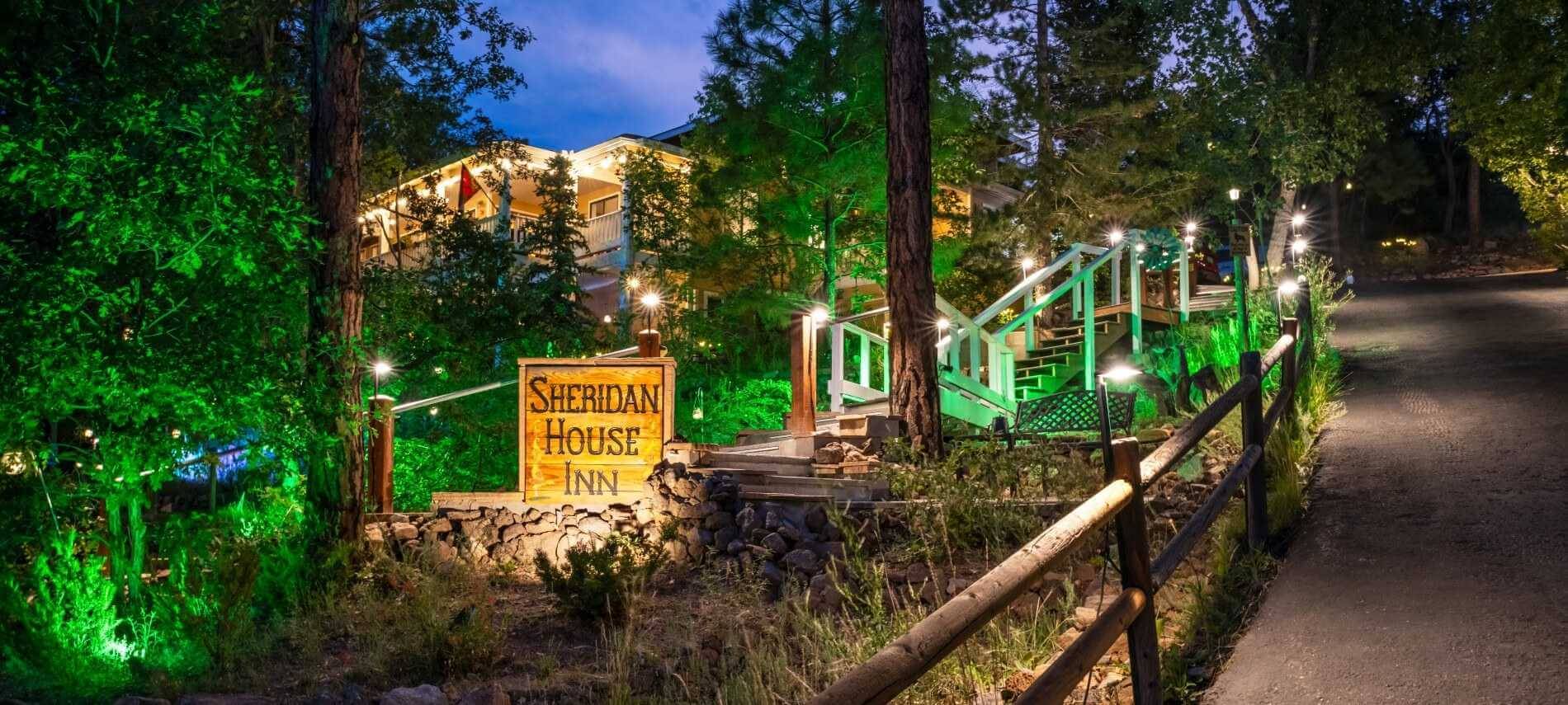 lighted up building in evening with big trees a stairway leading up to it, and green spotlights and a Sheridan House Inn sign