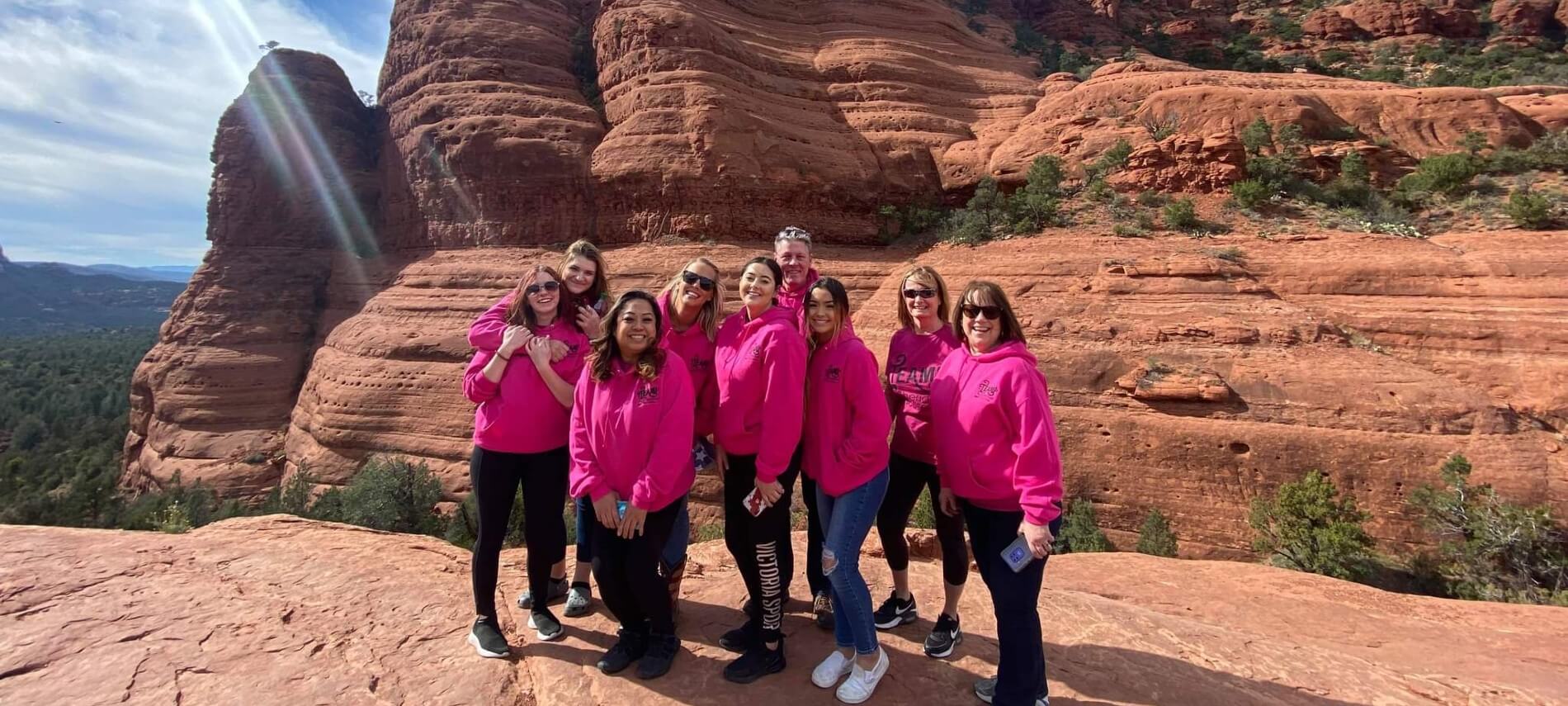 Group of 9 adults in pink hoodies standing in front of red rock formation