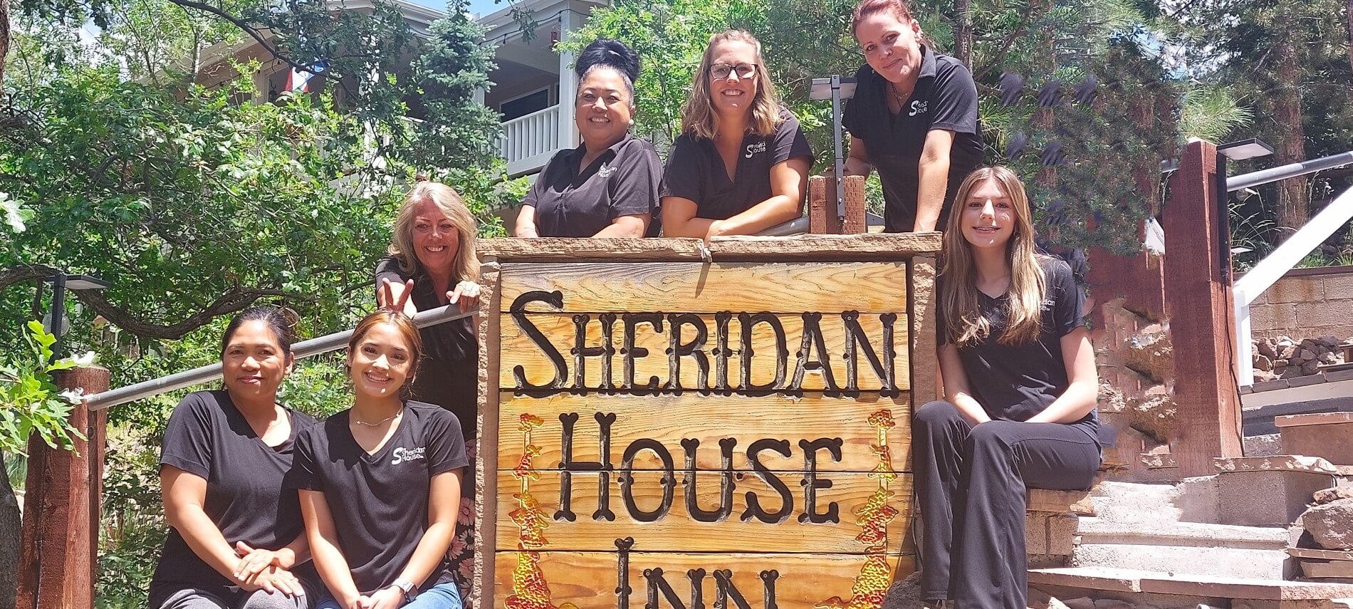 group of women in front of wooden Sheridan House Inn sign in front of a building in the forest
