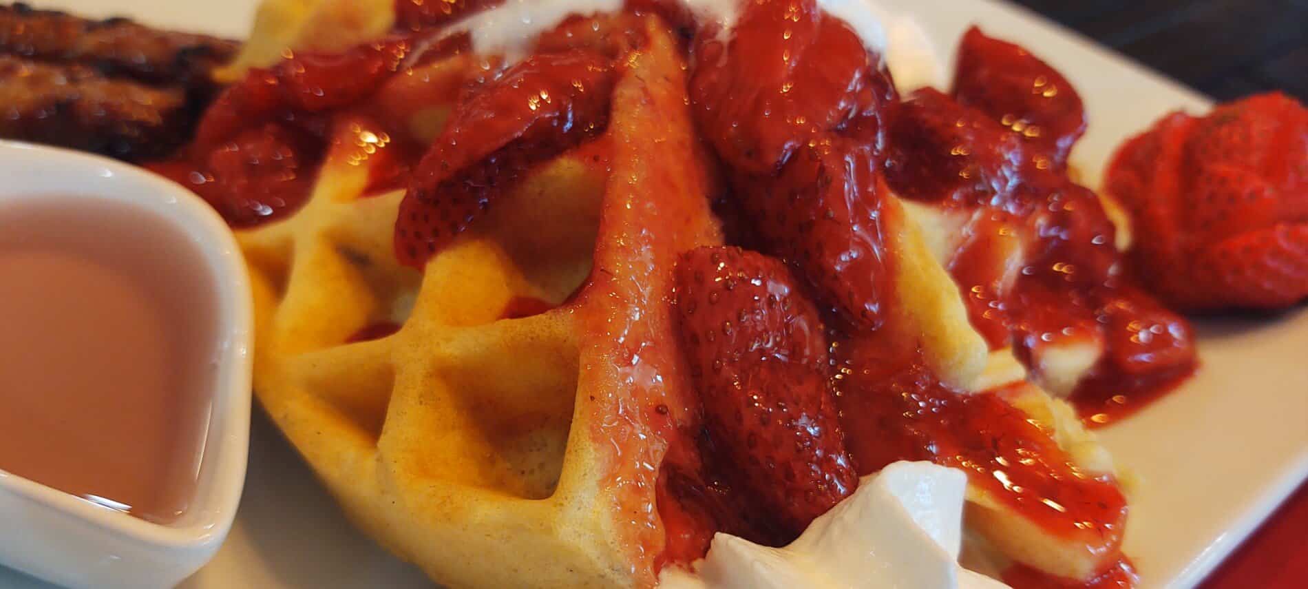 white plate with quartered belgion waffle with fresh strawberry sauce on top with a syrup boat