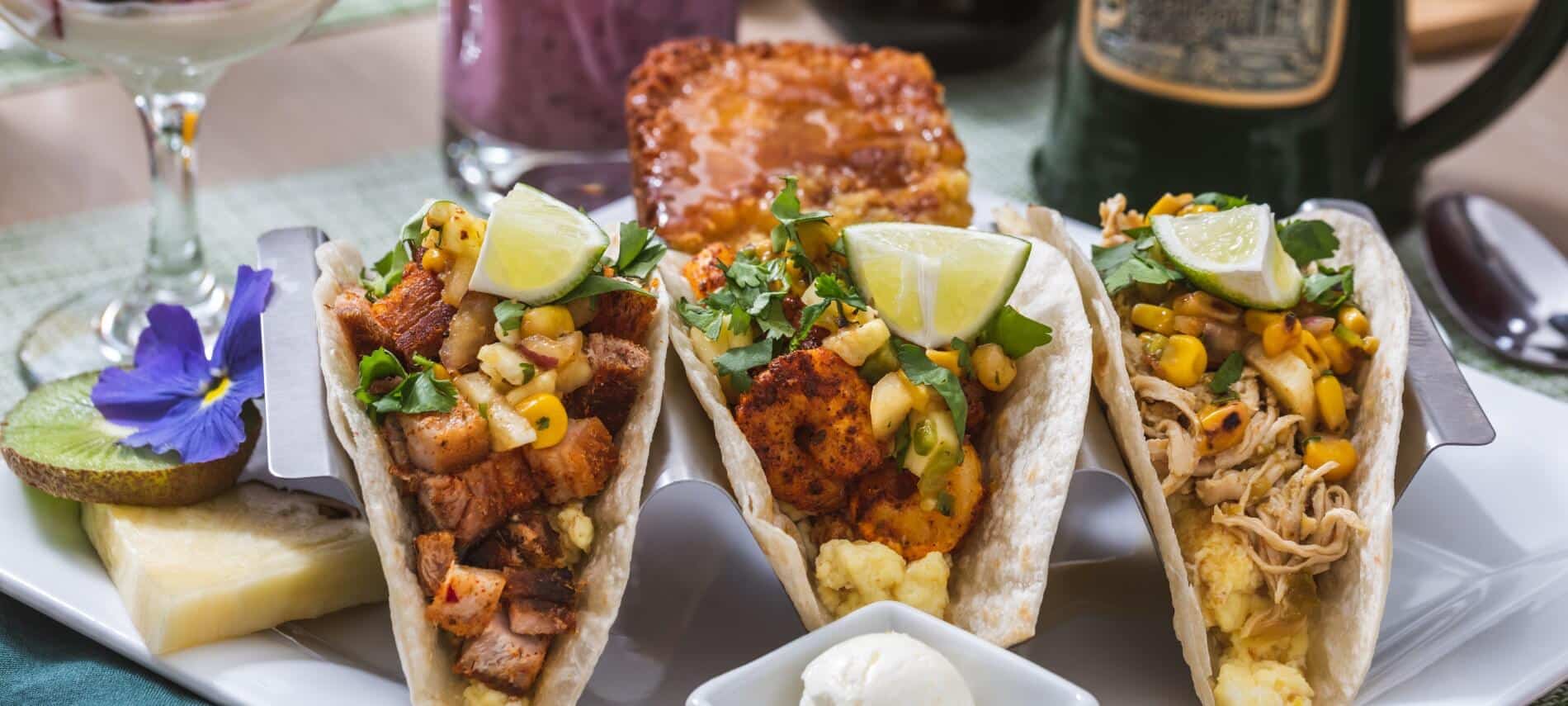 3 standing up taco shells with meat, scrambled eggs, corn salsa, cilantro and a lime wedge