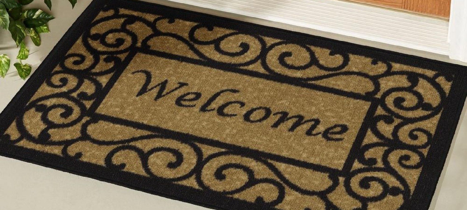 Large brown and black welcome mat with scroll design on the floor in front of a door